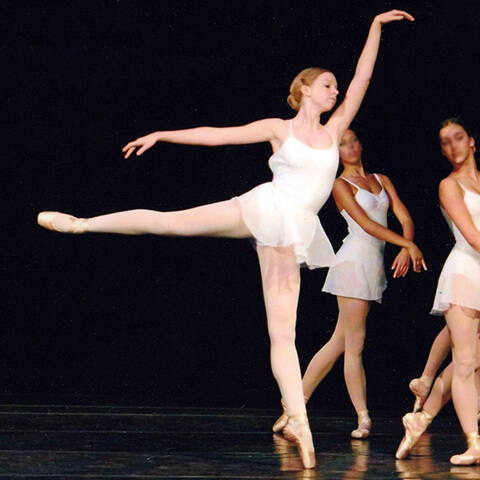 Susie performs an arabesque on pointe on stage in 2007 wearing a white leotard and skirt